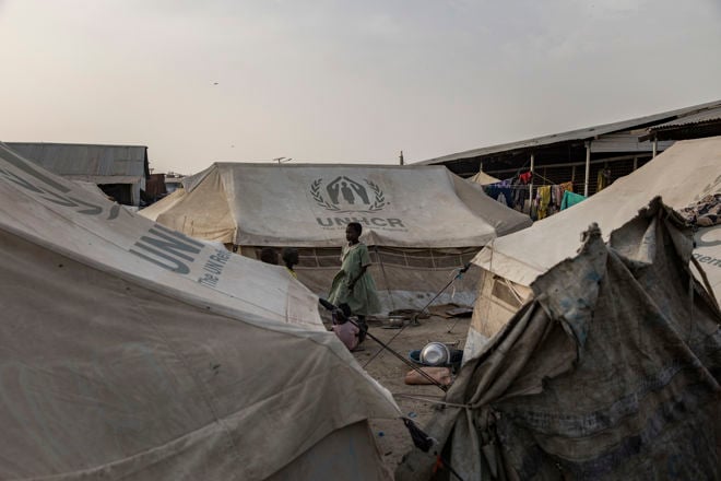 En kvinne og et barn står mellom UNHCR-telt i en flyktningleir, med klær som henger til tørk i bakgrunnen.