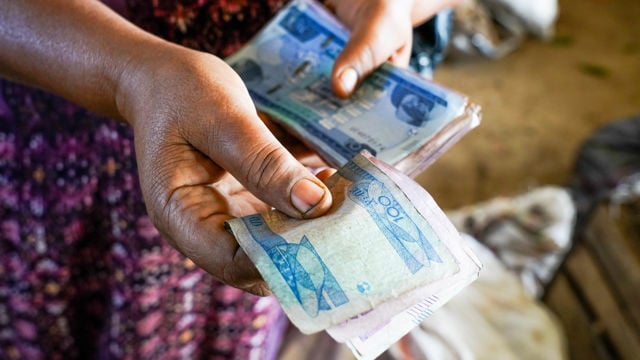 En kvinne med et lite barn på ryggen legger en stemmeseddel i en gjennomsiktig valgurne mens to valgfunksjonærer sitter ved siden av.